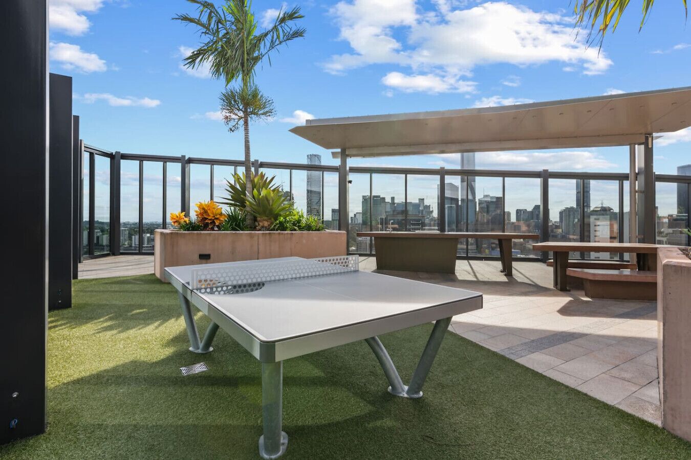 A rooftop terrace with a ping pong table, seating areas, and a view of the city skyline.