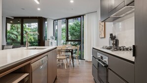 A modern kitchen with a large island, stainless steel appliances, and a view of greenery through large windows.