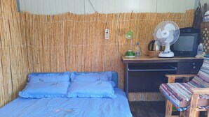 Una habitación con una cama, un escritorio con computadora, una silla y un ventilador.