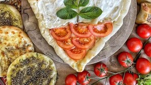 Una pizza con forma de corazón, adornada con rodajas de tomate y una hoja, rodeada de diversos alimentos y verduras frescas.