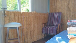 Una habitación con un separador de bambú, una escalera de madera, una silla estampada y una cama con colcha azul.