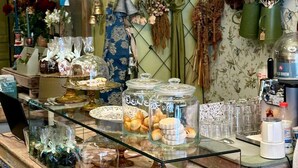 Mostrador de panadería con pasteles, una máquina de café y varias flores y plantas al fondo.