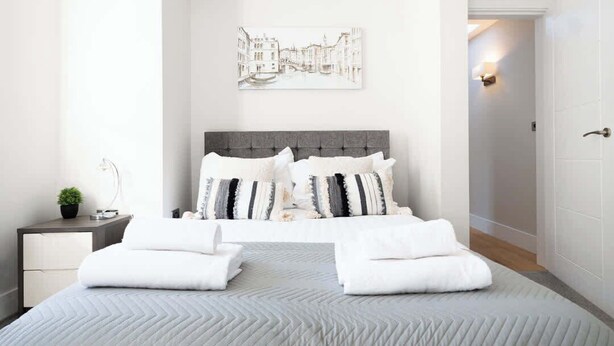 A modern bedroom with a bed, bedside tables, and a wall-mounted artwork. - Vineyard Style 2BR with Garden and Parking (Shudy Camps)