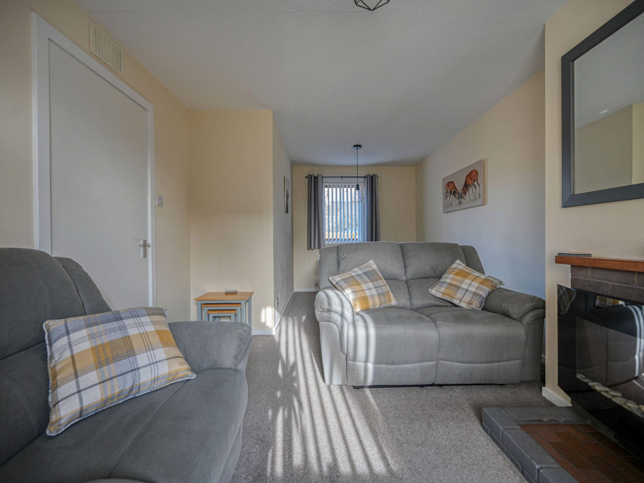 A living room with two grey sofas, each with plaid cushions, a small wooden table, and a fireplace.