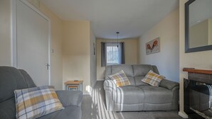 A living room with two grey sofas, each with plaid cushions, a small wooden table, and a fireplace.