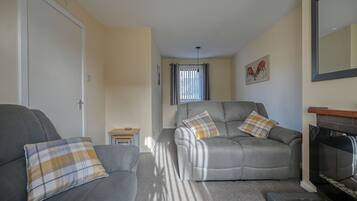 A living room with two grey sofas, each with plaid cushions, a small wooden table, and a fireplace.
