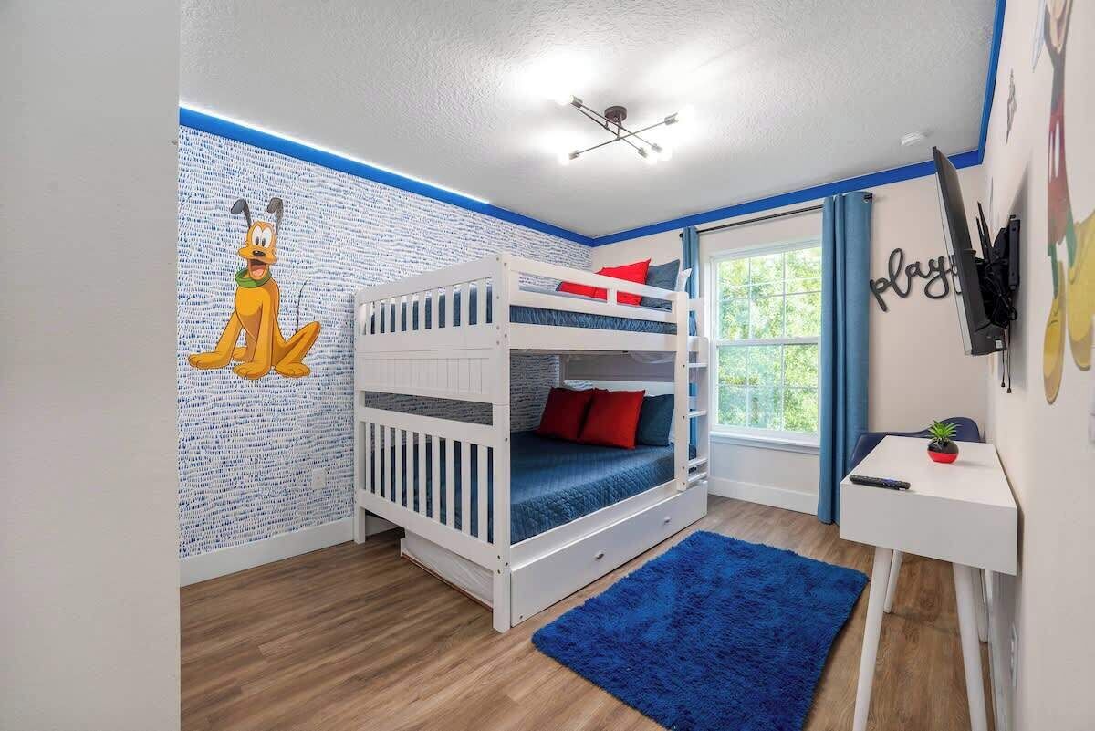 Een kinderkamer met stapelbedden, een blauw vloerkleed, een bureau en een muurschildering.
