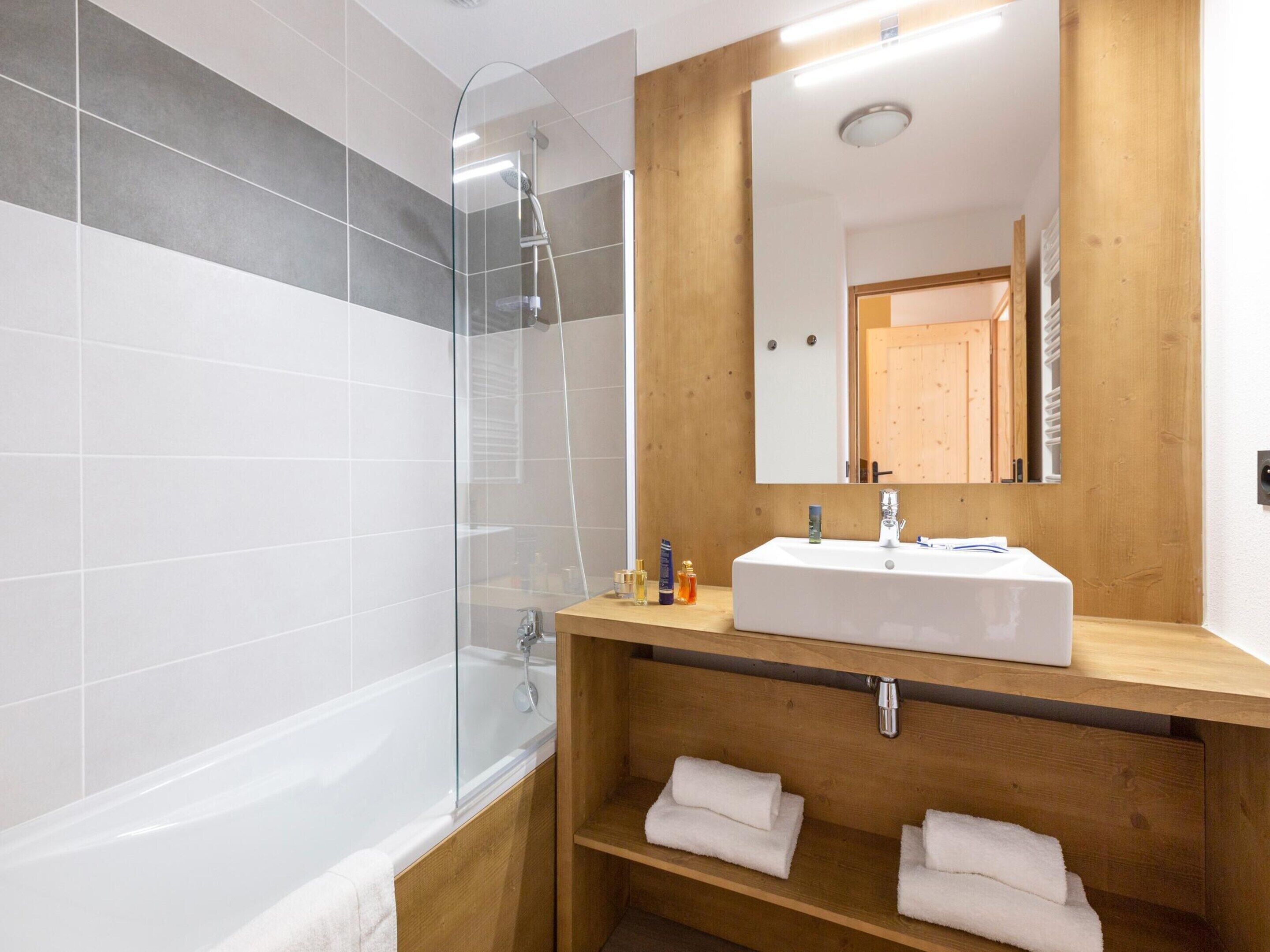 Un baño moderno con ducha de vidrio, lavamanos blanco y repisas de madera.