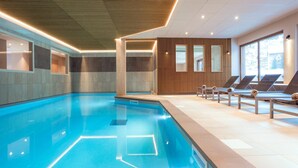 A modern indoor swimming pool with clear water, surrounded by lounge chairs and a wooden panel wall. - Apartment in Beaufort With Spa & Mountain Views (Beaufort)
