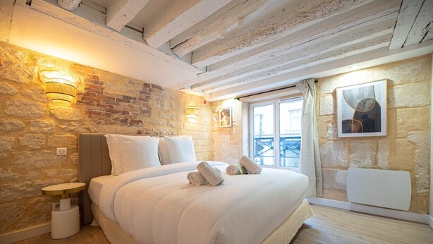 Une chambre avec un grand lit, des murs en pierre, un plafond en bois et une fenêtre donnant sur un paysage agréable.
