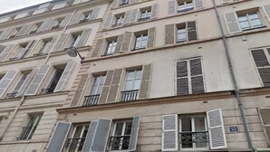 Un immeuble à plusieurs étages, doté de nombreuses fenêtres, dont certaines sont équipées de volets, et sur lequel on peut voir une enseigne indiquant l’adresse.