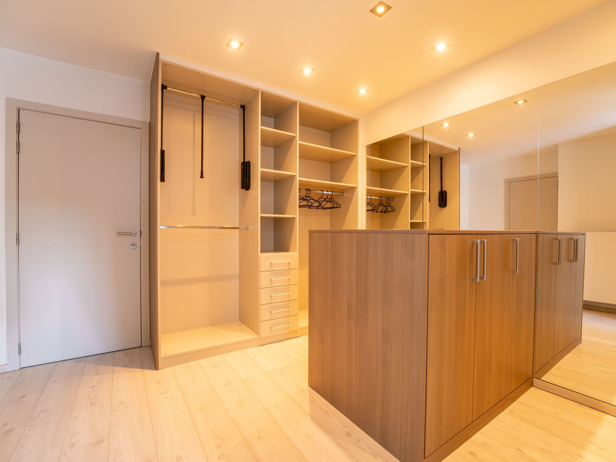 A spacious room with a large wooden wardrobe, a built-in closet with multiple shelves and hanging space, and a door with a handle.