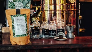A coffee shop counter with a bag of roasted coffee beans, a coffee grinder, and a large brewing kettle. - Mojigao Eco Resort (Assagao)