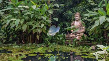 A seated statue surrounded by lush greenery and a pond with lily pads.