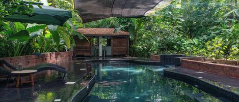 A pool area with a small building, lounge chairs, and surrounding greenery.