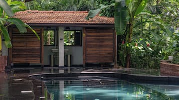 A pool area with a tiled roof structure, wooden shutters, and lush greenery.