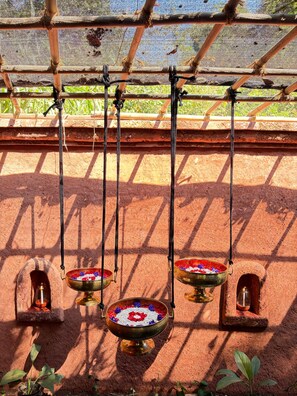 Una lámpara de latón colgante tradicional con decoraciones florales, suspendida por cuerdas de una estructura de madera.