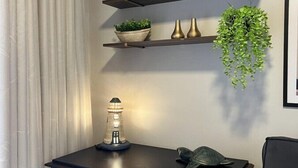 Een kamer met een blauwe kast, een wandplank met decoratieve objecten, een hangplant en een klein model van een vuurtoren.