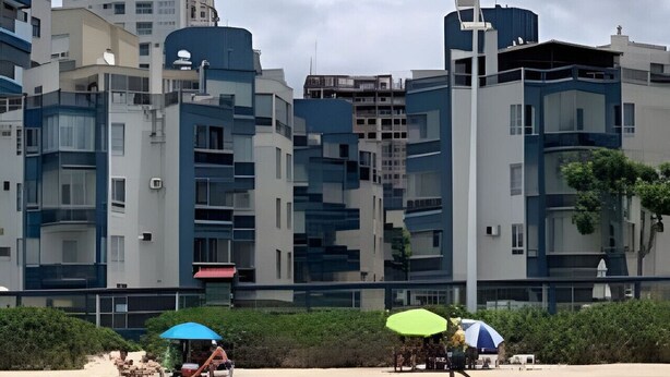 Een strand met moderne gebouwen op de achtergrond, een heldere lucht en een rustige zee.