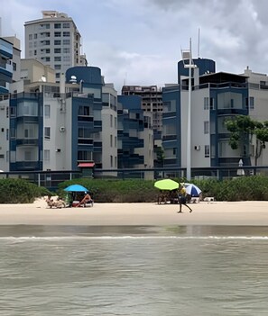 A beach with modern buildings in the background, a clear sky, and a calm sea. - Pé na Areia Itapema · 3 Quartos · Churrasqueira (Itapema)