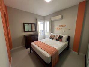 A bedroom with a bed, dresser, and a window with curtains. - Pé na Areia Itapema · 3 Quartos · Churrasqueira (Itapema)