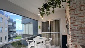 Een balkon met een tafel en stoelen, een hangplant en uitzicht op een gebouw.