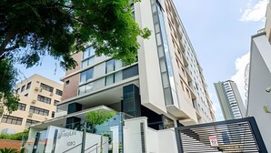 A modern building with a glass facade, a staircase leading to an upper level, and a gated entrance. - Apartamento completo na Av. Iguaçu — garagem, rooftop e localização estratégica (Curitiba)