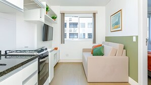 A modern kitchen with a gas stove, oven, and a flat-screen TV. There is a window with a view of buildings outside. - Apartamento completo na Av. Iguaçu — garagem, rooftop e localização estratégica (Curitiba)