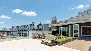 A rooftop terrace with a city skyline in the background, a covered seating area, and a small garden. - Apartamento completo na Av. Iguaçu — garagem, rooftop e localização estratégica (Curitiba)