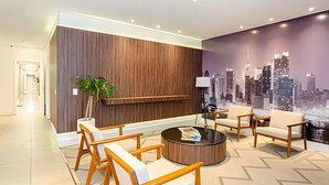 Un moderno lobby con mostrador de recepción, zona de estar y un mural con vistas a la ciudad.