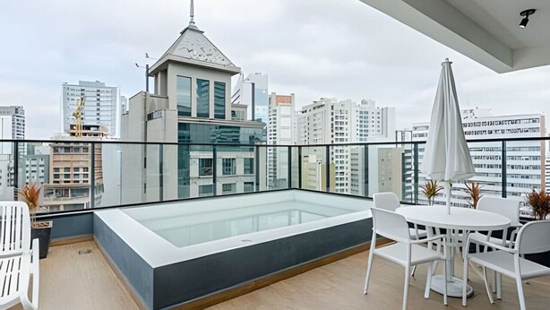 A rooftop terrace with a glass-enclosed pool, white furniture, and a city view.