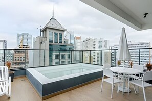 Une terrasse sur le toit avec une piscine à moitié couverte par une verrière, des meubles blancs et une vue sur la ville.