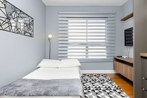 Une chambre à coucher moderne avec un lit, un tapis à motifs géométriques, une œuvre d’art représentant une carte du monde, une lampe sur pied et un téléviseur posé sur une étagère en bois.
