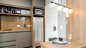 A compact kitchen with a microwave, toaster, and refrigerator, a dining area with a table and chairs, and a wall-mounted light fixture.