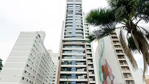 Un edifici alt i modern amb diverses plantes, que destaca un element vertical central i un mural de colors a una banda.