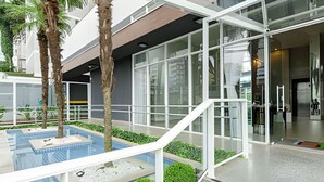 Un edifici modern amb grans finestres de vidre, una zona de piscina amb palmeres i una escala que condueix a l'entrada.