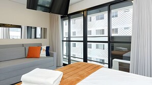 Habitació d'hotel moderna amb una finestra gran, un llit, un sofà i un televisió de pantalla plana penjada a la paret.