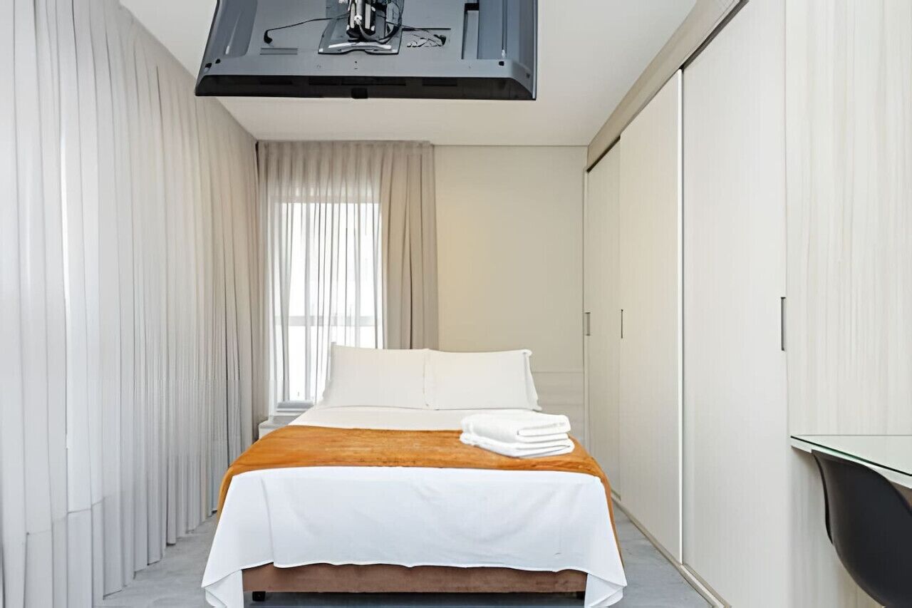 A modern hotel room with a bed, a flat-screen TV, and a large window with curtains.