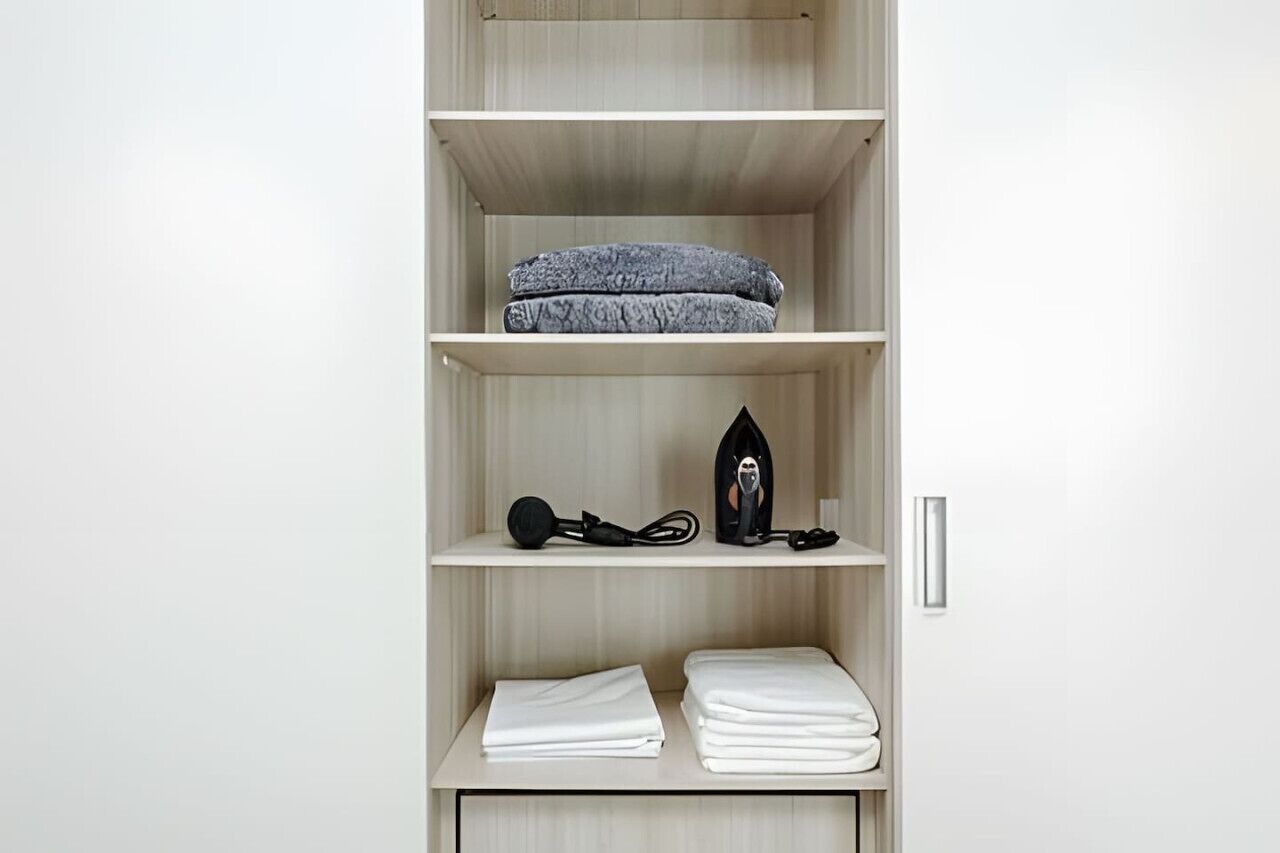Guarda-roupa com prateleiras contendo roupas dobradas, um secador de cabelo e um ferro.