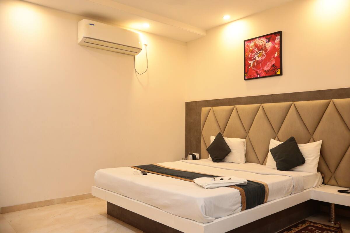 Habitación de hotel con cama, mesita de noche, aire acondicionado y un cuadro en la pared.