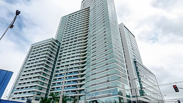 A modern high-rise building with a unique angular design, featuring multiple balconies and large windows. - Studio Central no Prédio 7Th Avenue, com ar e vaga (Curitiba)