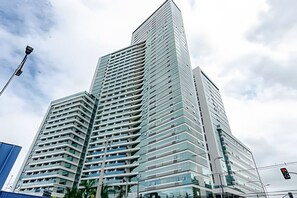 A modern high-rise building with a unique angular design, featuring multiple balconies and large windows. - Studio Central no Prédio 7Th Avenue, com ar e vaga (Curitiba)