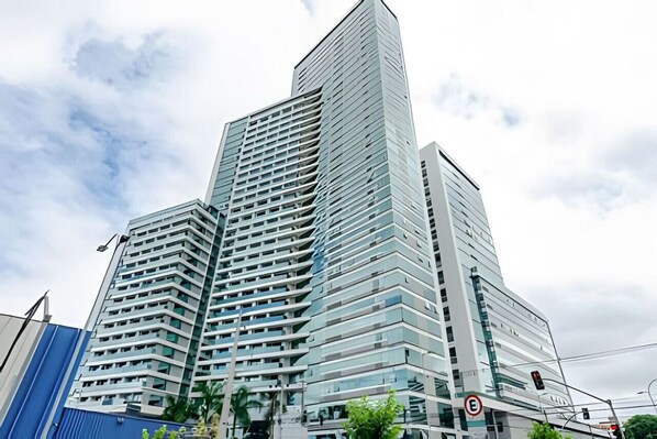 A modern high-rise building with a glass facade and multiple balconies. - Studio Central no Prédio 7Th Avenue, com ar e vaga (Curitiba)