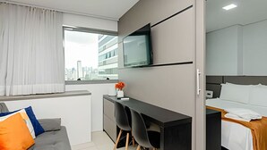A modern hotel room with a bed, a desk, and a TV mounted on the wall. - Studio Central no Prédio 7Th Avenue, com ar e vaga (Curitiba)