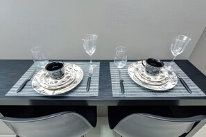 A dining table set with two plates, cutlery, and wine glasses. - Studio Central no Prédio 7Th Avenue, com ar e vaga (Curitiba)