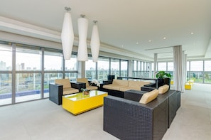 Lounge do rooftop: sofas de rata, mesa amarela e vista 360 graus da cidade - 7th Avenue Studio · 15º andar · Vista e Garagem (Curitiba)