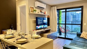 Un saló modern amb zona de menjador, televisió de pantalla plana i una finestra gran amb vista a la ciutat.