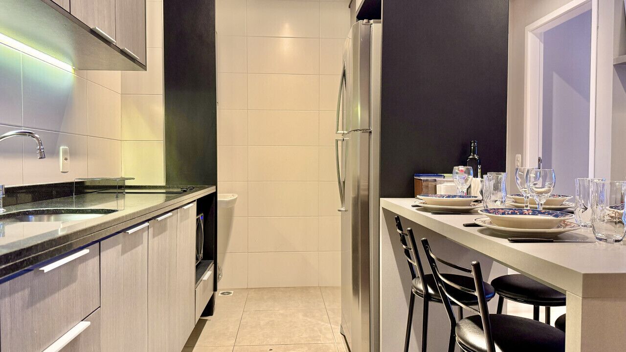 A modern kitchen with a built-in refrigerator, a sink, and a dining area with chairs and a table set for two.