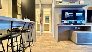 Una cuina moderna amb zona de bar, televisió que mostra serveis de streaming i un passadís que condueix a un bany.