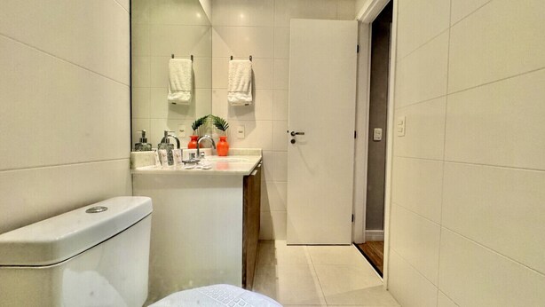 A bathroom with a toilet, sink, and mirror. There are towels hanging on the wall and a door leading to another room.